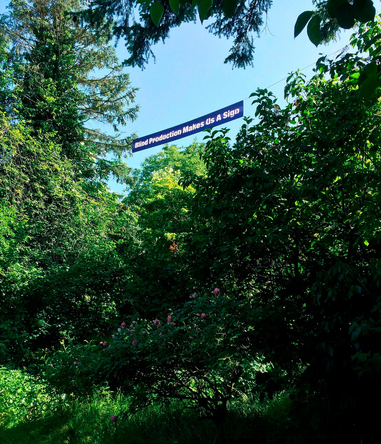 Banner Blind Production Makes Us A Sign hängt in grünem Ausstellungsgelände  Fotografie von Heiko Schäfer