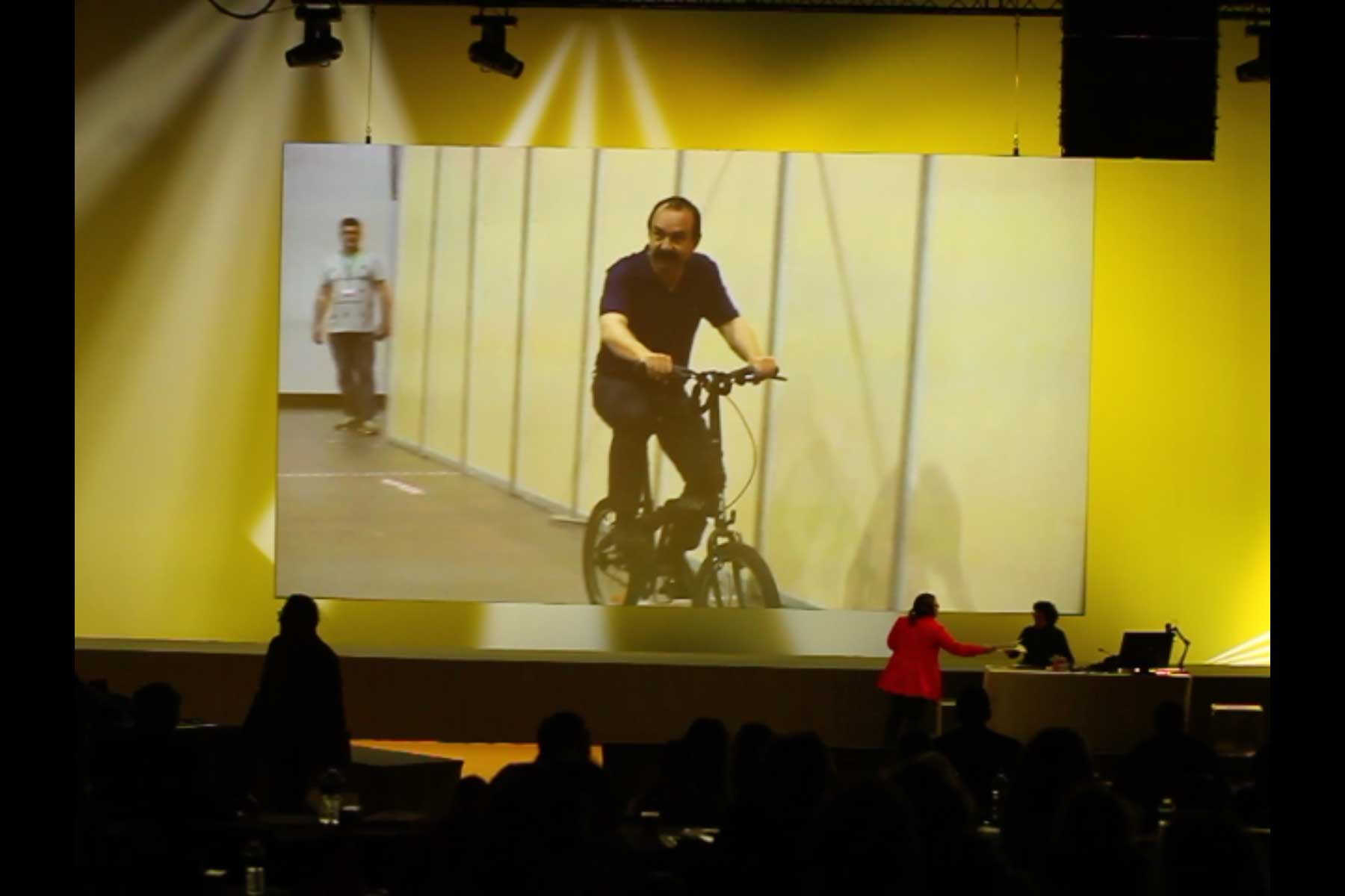 Projektion, die den Generalsekretär der CGT, Philippe Martinez, auf einem Klapprad in den Gängen der Messehallen in Marseille  Fotografie von Heiko Schäfer