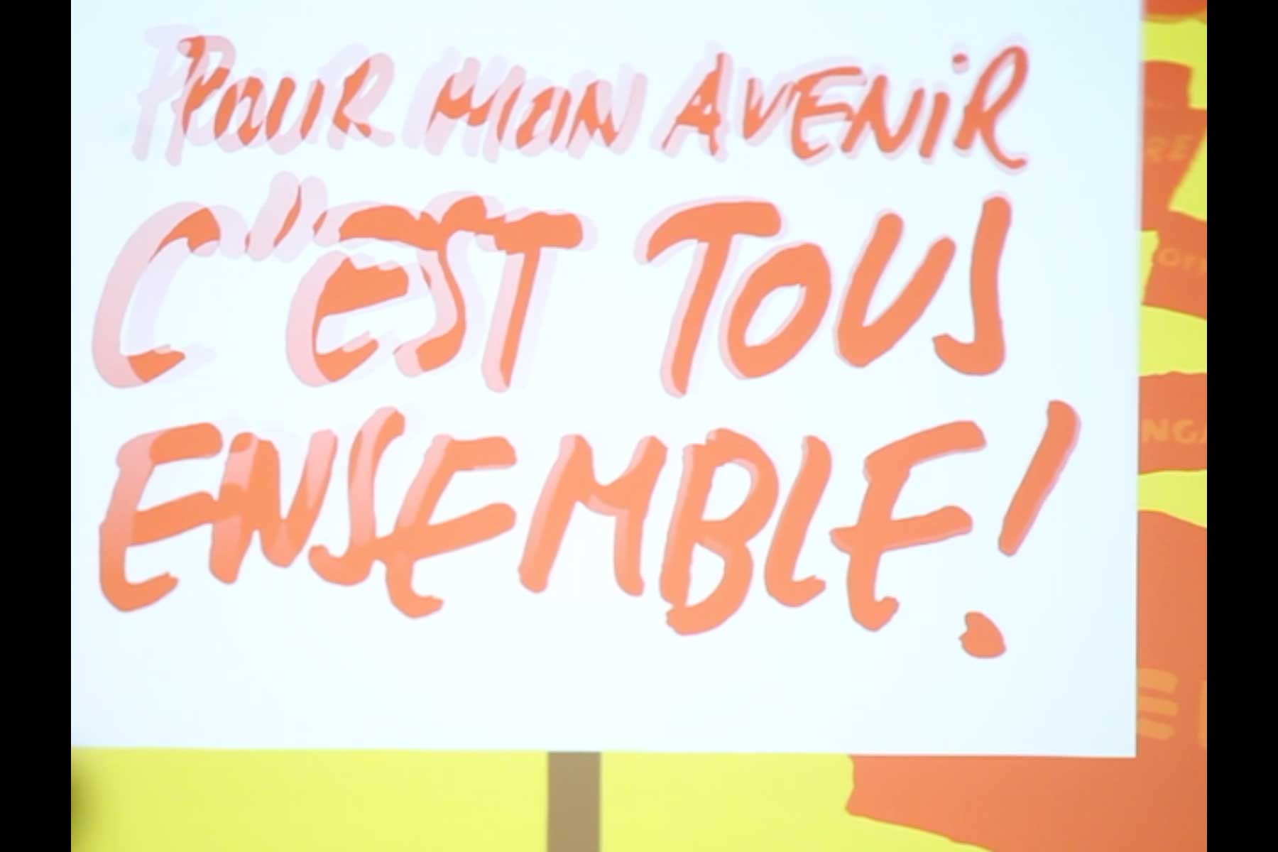 Projektion mit einer Grafik in rot und gelb, die den Slogan 