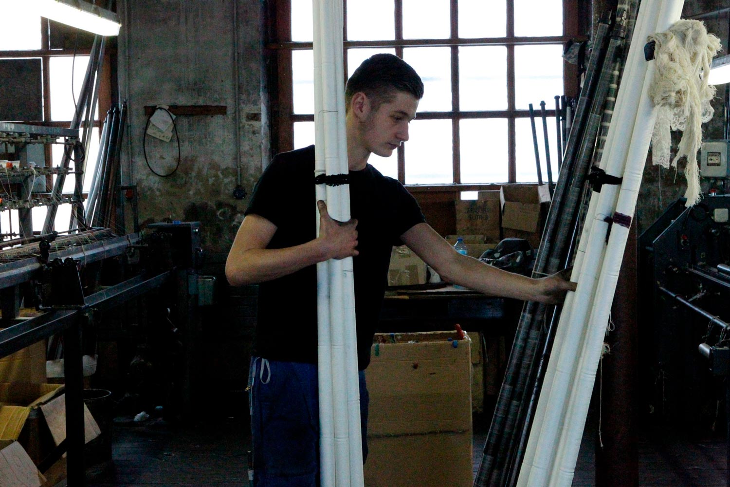 Der junge Textilarbeiter Matthieu trägt Textilspulen in der Textilfirma Codentel  Fotografie von Heiko Schäfer