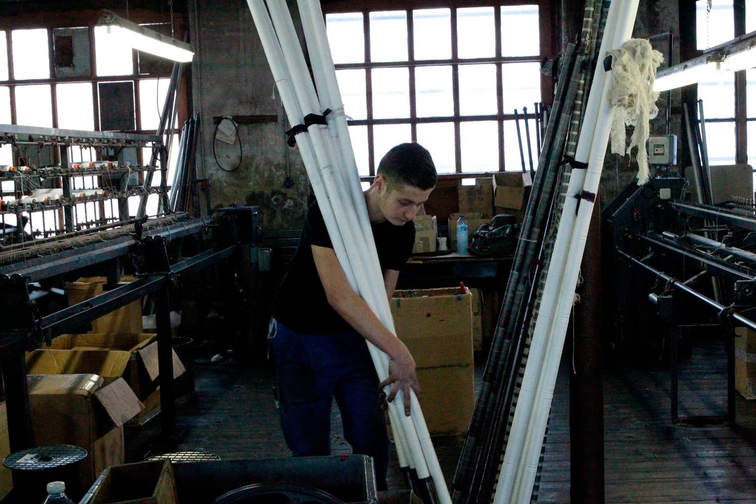 Der junge Textilarbeiter Matthieu trägt Textilspulen in der Textilfirma Codentel  Fotografie von Heiko Schäfer