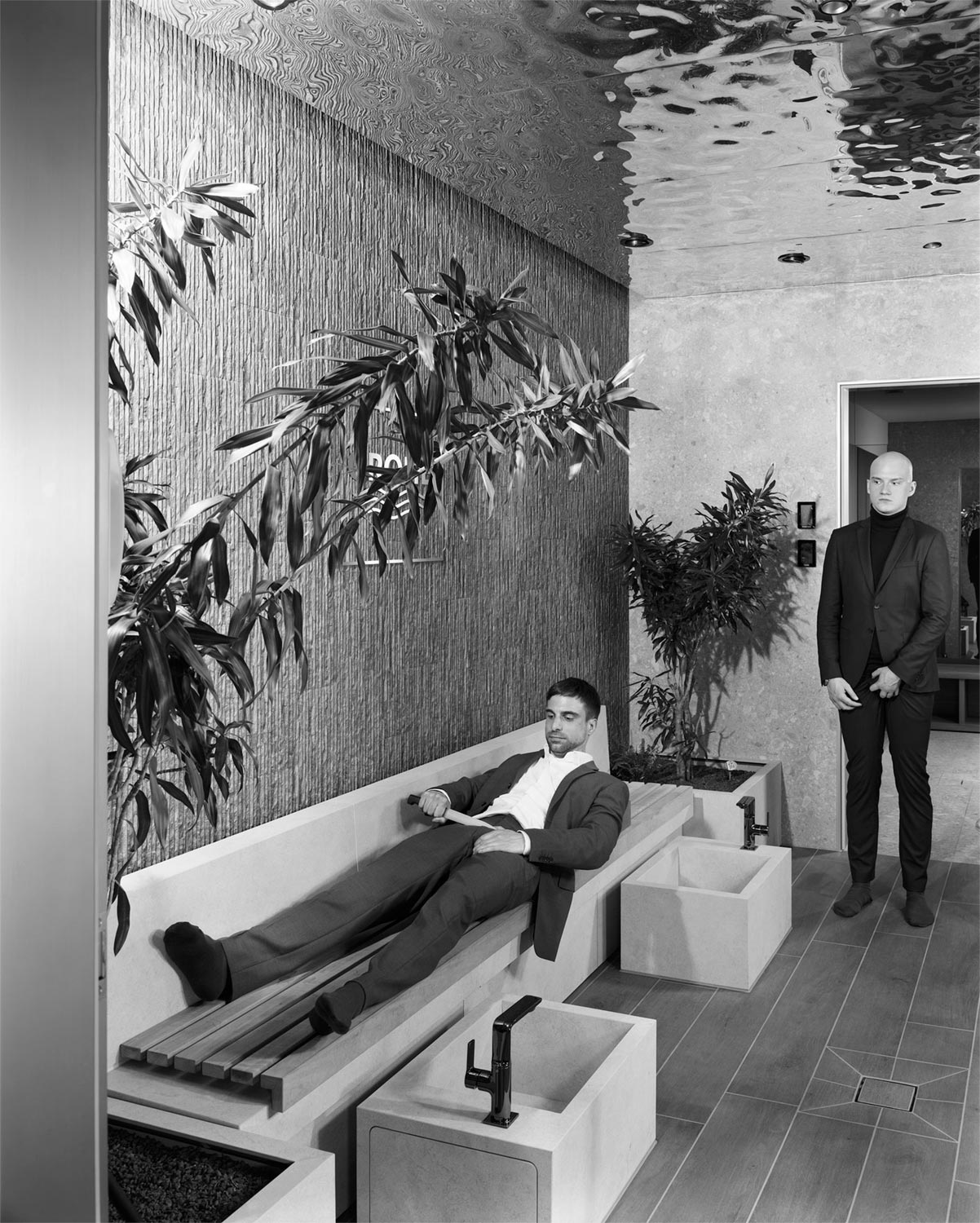 Ein Mann in Anzug kastriert sich in einem Spa, ein anderer schaut zu  Fotografie von Heiko Schäfer